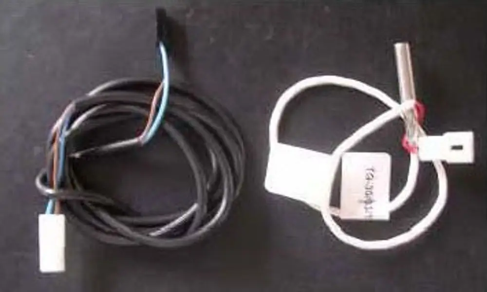 Zwei Hochtemperaturfühler mit verschiedenen Kabeln. Links ein schwarzes Kabel, rechts ein weißes Kabel mit einem metallischen Sensor. Beide Komponenten stammen von Remeha.